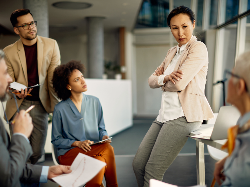 Manager leading her employees, leaning on a table